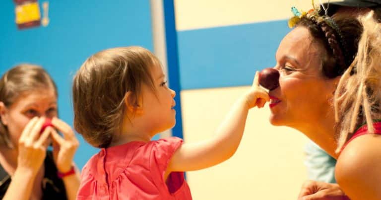 Enfant hospitalisée posant un nez rouge sur une clown du Rire Médecin, moment de joie à l’hôpital