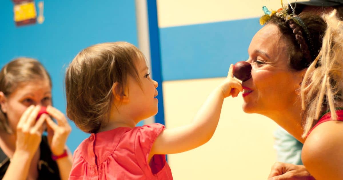 Enfant hospitalisée posant un nez rouge sur une clown du Rire Médecin, moment de joie à l’hôpital