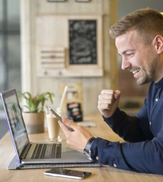 Happy freelancer with tablet and laptop computer in coffee shop.